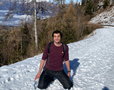 Hasan kneeling in deep snow on a mountain path, smiling, with clear sky and mountains in the background, symbolizing his Everest dream
