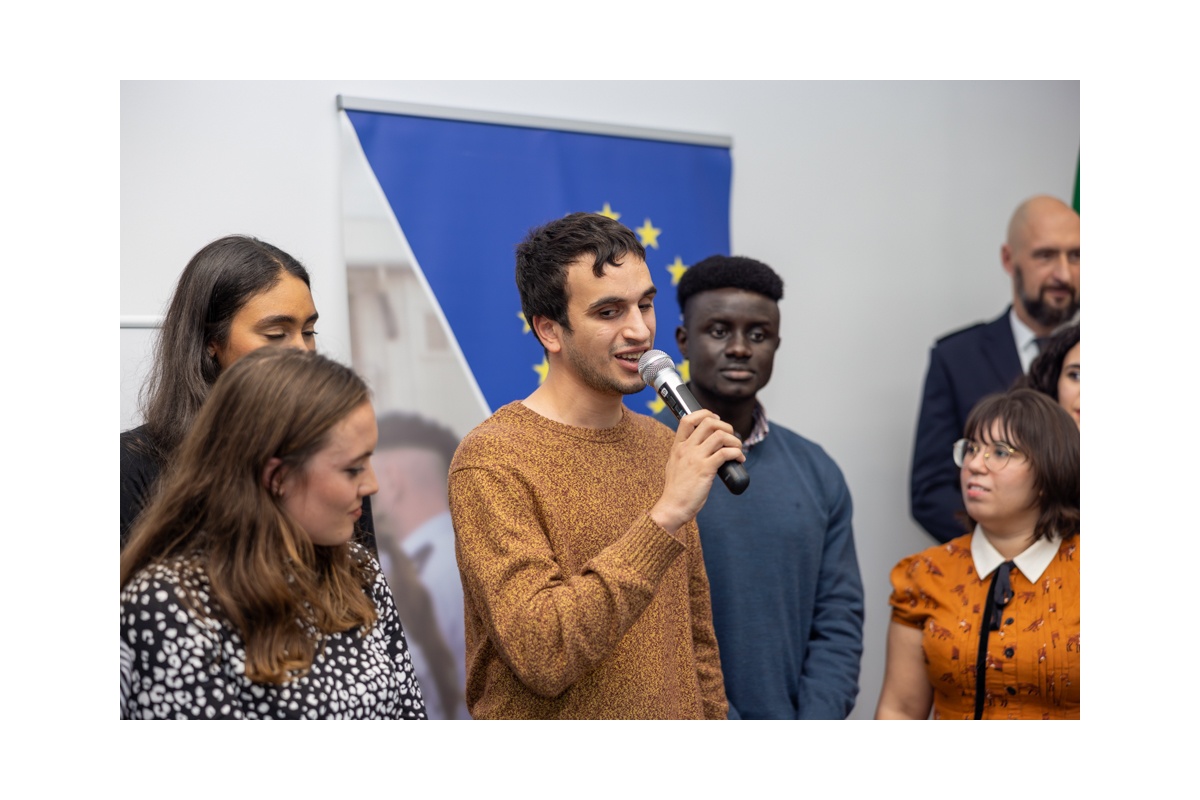Hasan is speaking into a microphone at an OSCE event, surrounded by fellow youth leaders